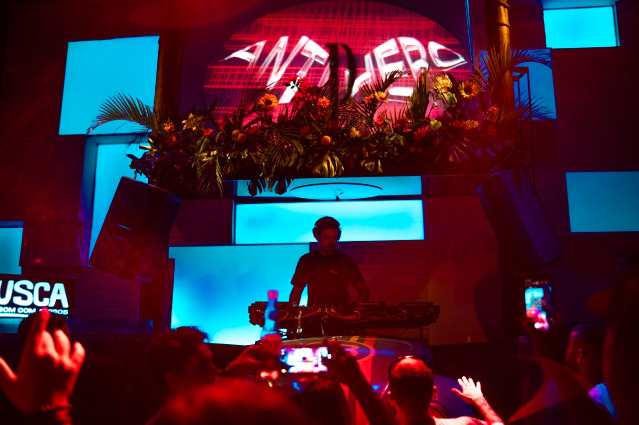 Palco com o logo ANTI HERO iluminado e o público de celulares erguidos